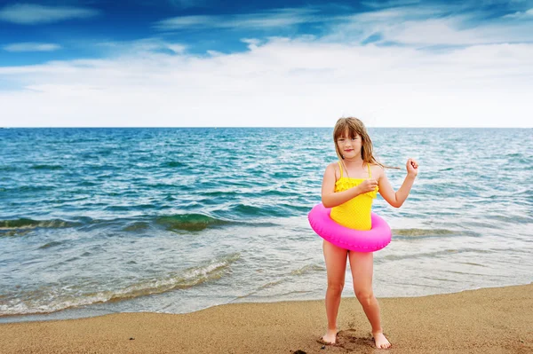 Adorable little girl in yellow swimming suit with pink inflatable ring by the sea on summer vacation