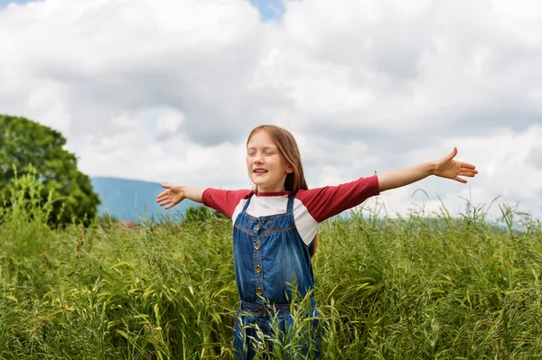 Little girl playing in green wheat field in summertime, wearing red and white t-shirt and overalls, arms wide open
