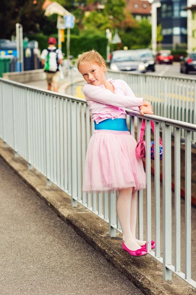 Outdoor portrait of a cute little girl of 7 years old, walking to dance school and dancing in the street, wearing dance skirt tutu