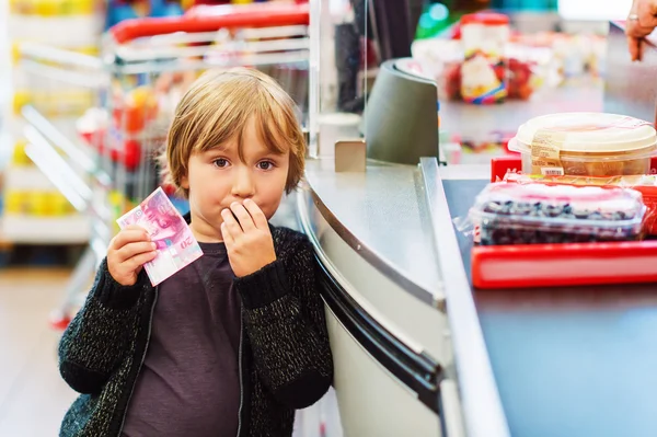 Little boy buying fruits in a food store, holding 20 chf bill