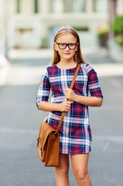 Pretty little 9 year old girl walking back to school, wearing glasses, plaid dress and brown leather bag