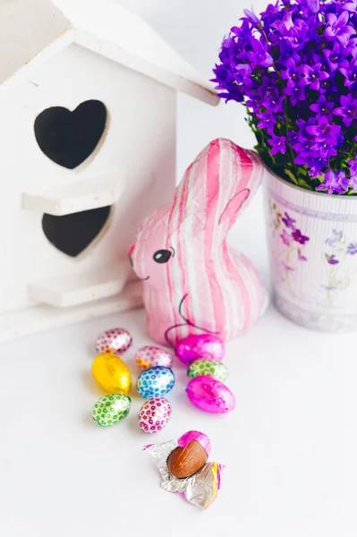 Colorful easter decoration with chocolate eggs, bunny, purple bell flowers and white bird house