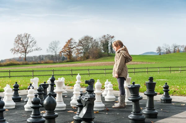 Adorable little girl playing with huge chess in a park on a cold day
