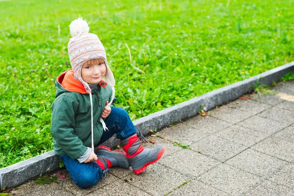 Outdoor portrait of a cute little boy of 3 years old, wearing warm coat, hat and boots