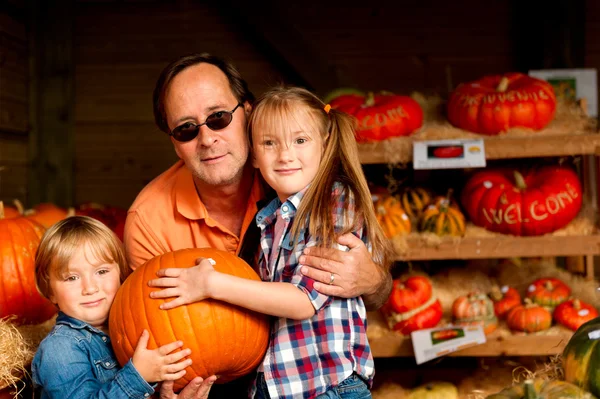 Father and two kids picking out pumpkin on the farm market