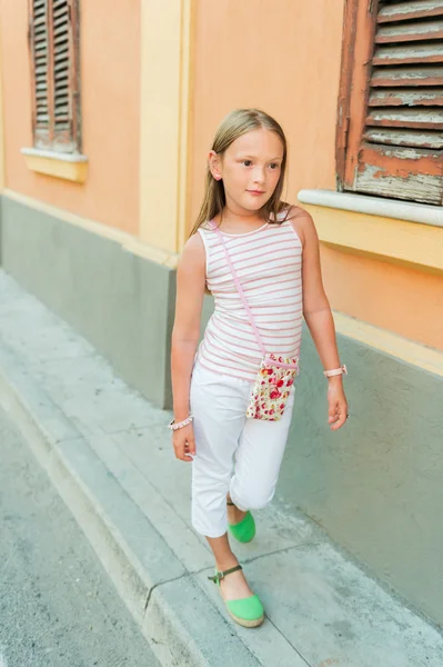 Outdoor portrait of a cute fashion little girl wearing white trousers and green shoes