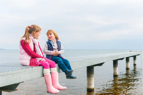 Cute kids playing by the lake, resting on a pier, wearing rain boots