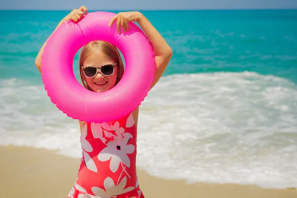 Adorable little girl with pink inflatable ring by the sea on summer vacation