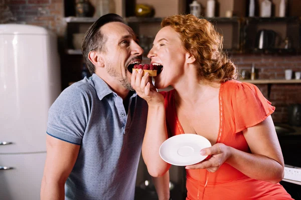 Man and woman biting cake