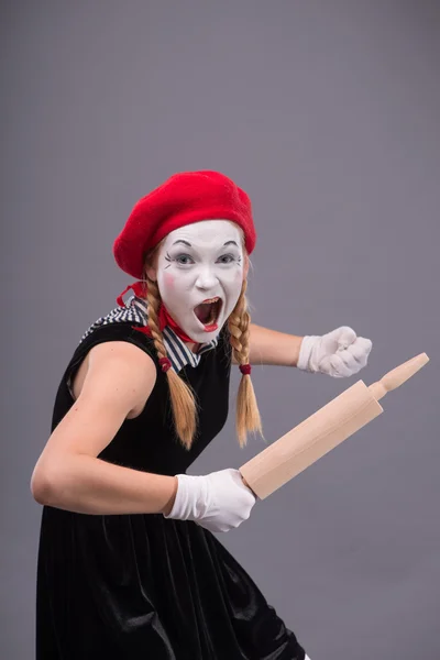 Portrait of female mime with red hat and white face grimacing wi