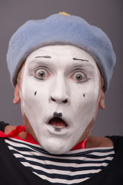 Portrait of young male mime with white face, grey hat showing em