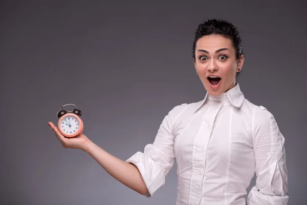 Portrait of pretty girl holding an alarm clock in her hand showi