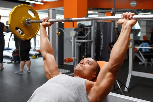 Lying man lifting barbell in gym