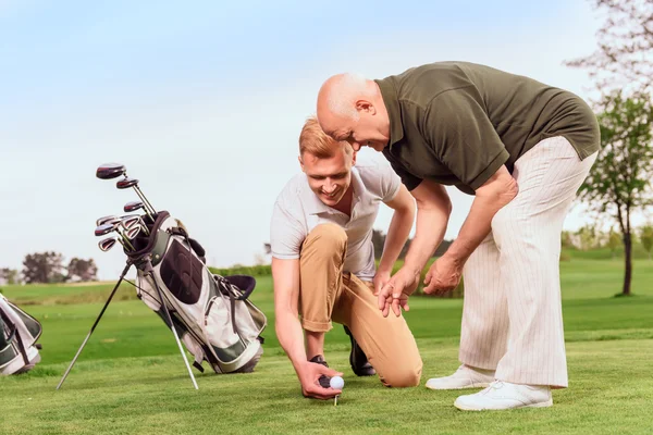 Two men putting ball on tee at course