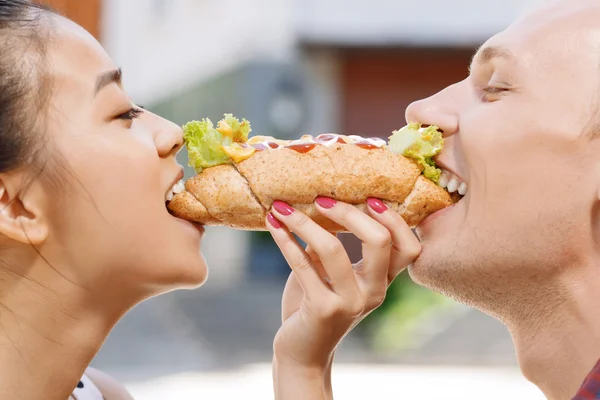 Man and woman biting same hotdog
