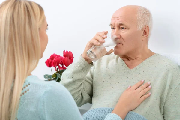 Elderly man drinks water given by granddaughter.