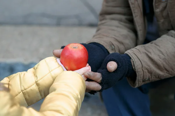 Child gives apple to the beggar.