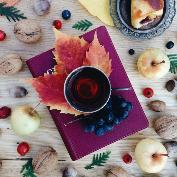 Cup of tea, book, leaves and autumn fruits on wooden background