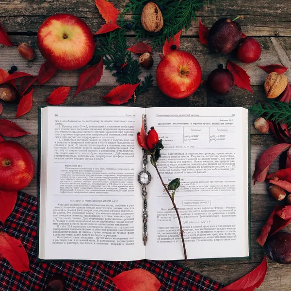 Wrist watch in open book, apples and autumn leaves on wooden background