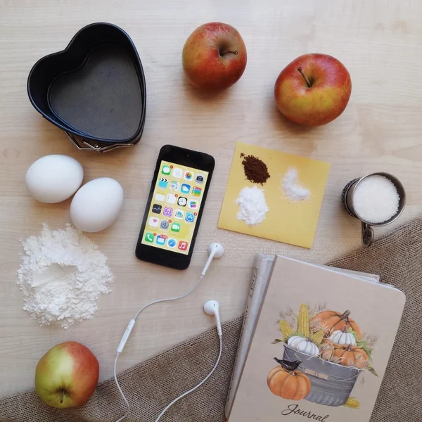 Music in smartphone and ingredients for apple pie on wooden background