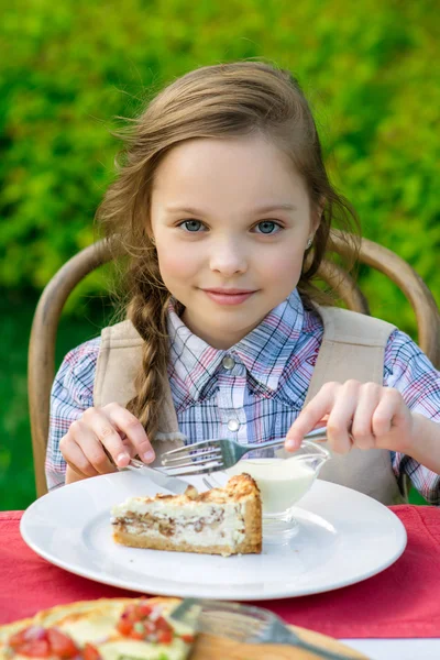 Cute little girl sitting by dinner table and eating