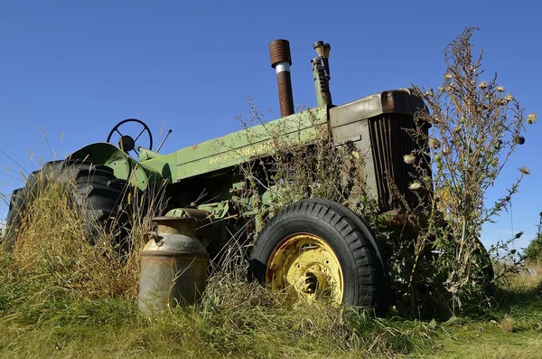 An old John Deere attractor and milk can in the weeds