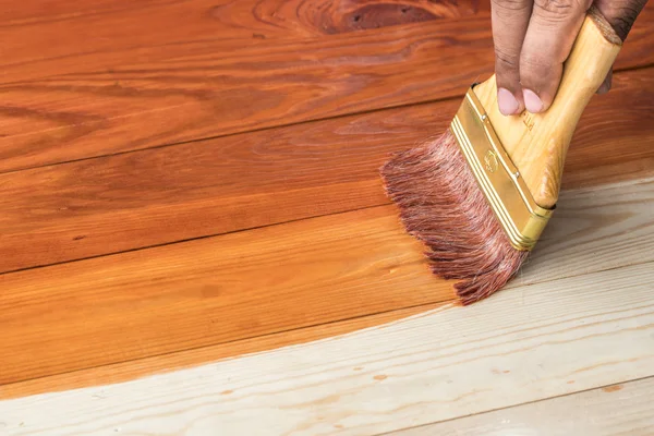 Hand holding a brush applying varnish paint on a wooden surface