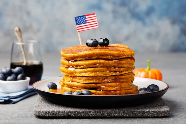 Pumpkin pancakes with maple syrup and blueberries on a plate with American flag on top
