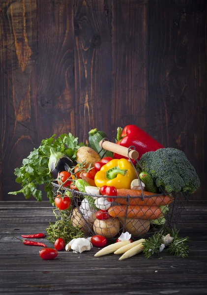 Vegetables variety in a wire basket on wooden background.