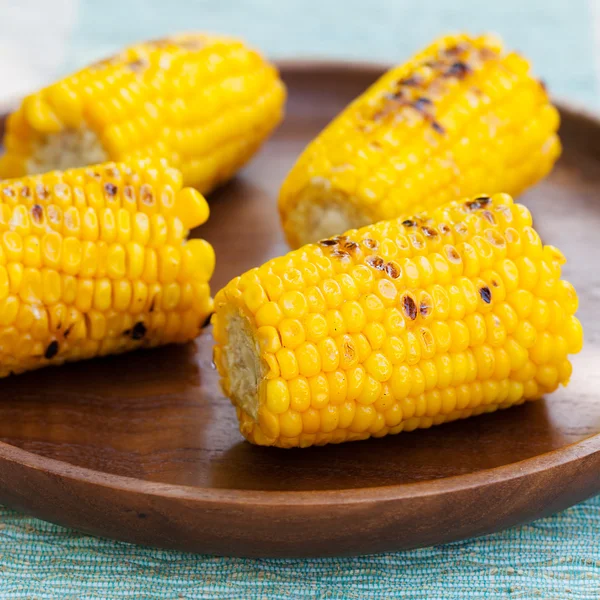 Grilled corn on the cob with salt and butter on a wooden plate
