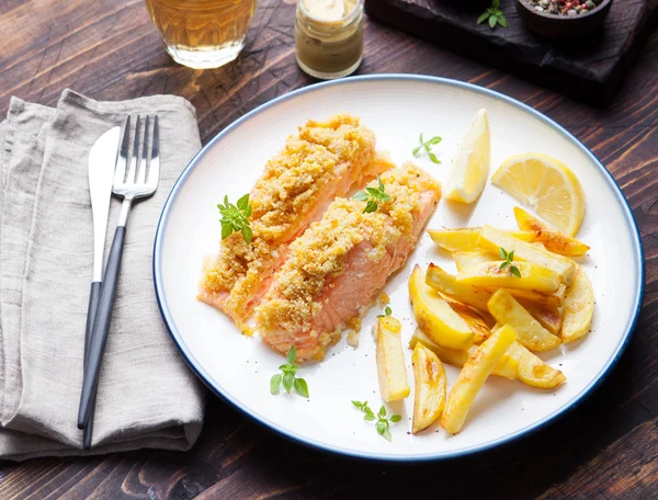 Fish salmon with crumple on top with baked potatoes and lemon slices on a wooden background