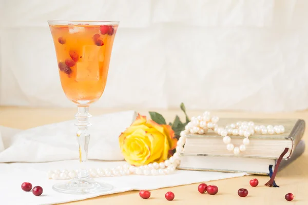 Glass of cranberry cocktail with vintage books and pearls