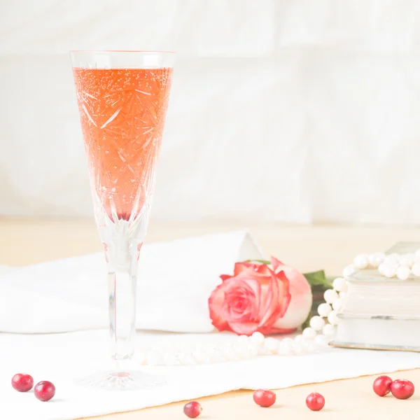 Glass of kir royal cocktail with vintage books and pearls