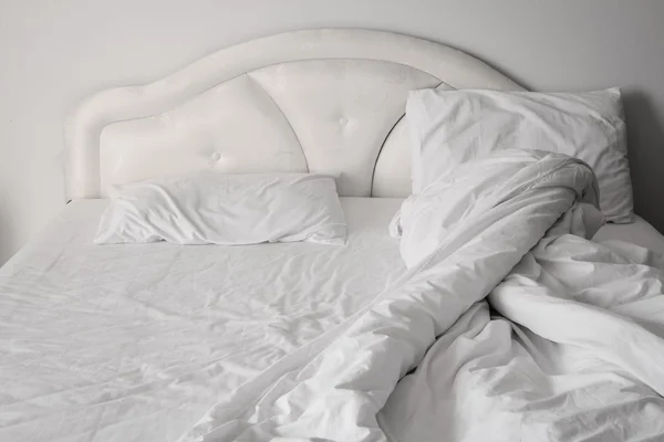 Unmade comfortable bed is strewn with white pillows.