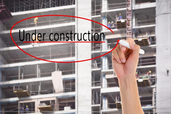 Hand write Under construction on blurred background of construction worker building on a scaffold