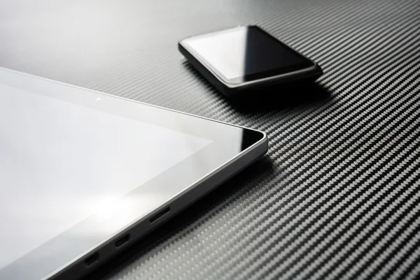 Business Mobile With Reflection Lying Next To Blank Tablet On A Carbon Layer