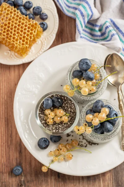 Milk pudding with chia seeds, blueberries and currants in a batch jars on wooden background
