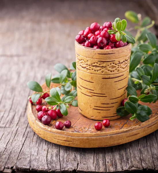 Fresh forest berries and lingonberry twigs in cup of birch bark on a wooden background.