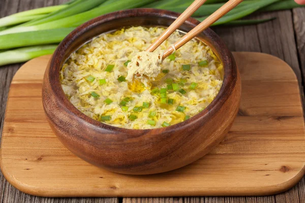 Chopsticks in bowl with traditional egg drop soup asian appetizer meal on wooden desk