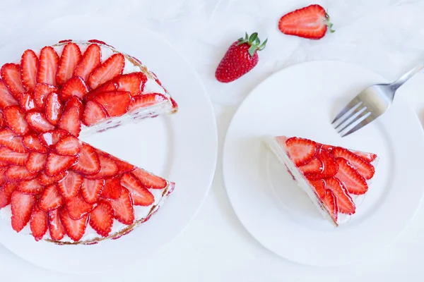 Sliced piece of gourmet homemade celebration strawberry cake sweet dessert food with whipped cream and fresh strawberries on white kitchen table background