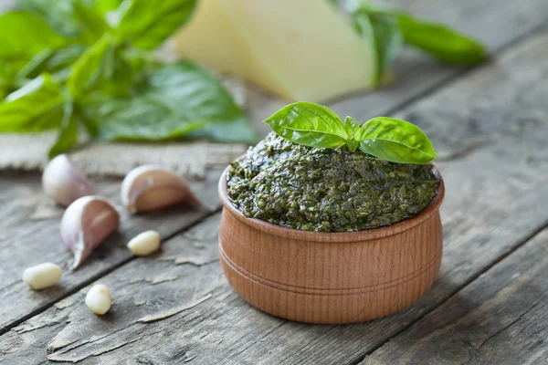 Wooden bowl of traditional Italian sauce pesto with parmesan, basil, nuts, garlic and olive oil. Vintage table background.