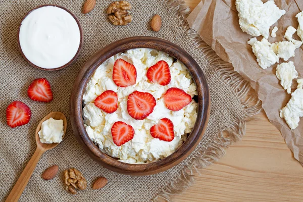 Cottage cheese healthy breakfast food with sour cream, fresh strawberry and nuts in rustic wooden dish on vintage kitchen table background
