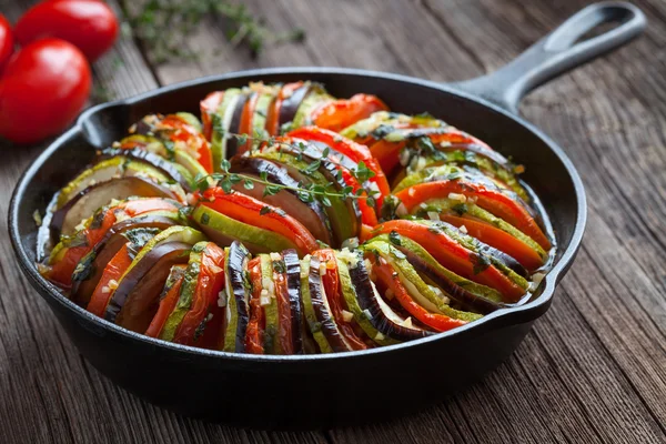 Traditional homemade vegetable ratatouille baked in cast iron frying pan healthy diet french vegetarian food on vintage wooden table background.