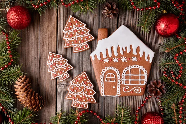 Christmas gingerbread house and fur tree cookies composition with xmas decorations on vintage wooden table background. Homemade traditional dessert food recipe.