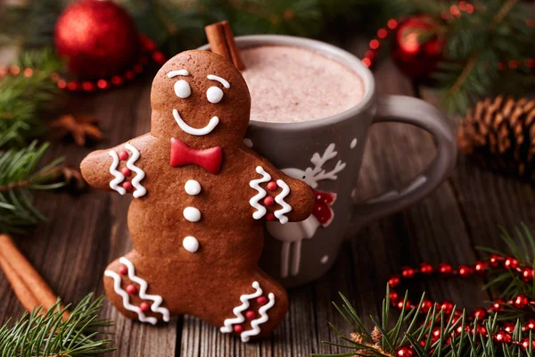 Cup of hot chocolate or cocoa with cinnamon and gingerbread man cookie in new year tree decorations frame on vintage wooden table background. Homemade traditional celebration recipe.