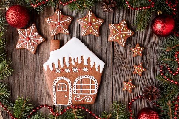 Gingerbread house and star cookies christmas composition in new year tree decorations frame on vintage wooden table background. Top view. Traditional homemade holiday recipe.