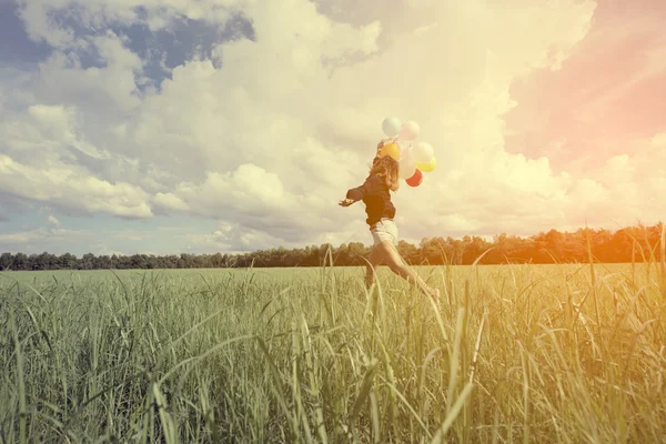 girl walking in a field letting go of a bunch of balloons done with a vintage retro instagram filter effect