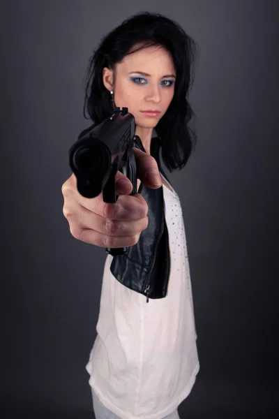 Pretty girl in leather jacket with gun in hands on a gray background