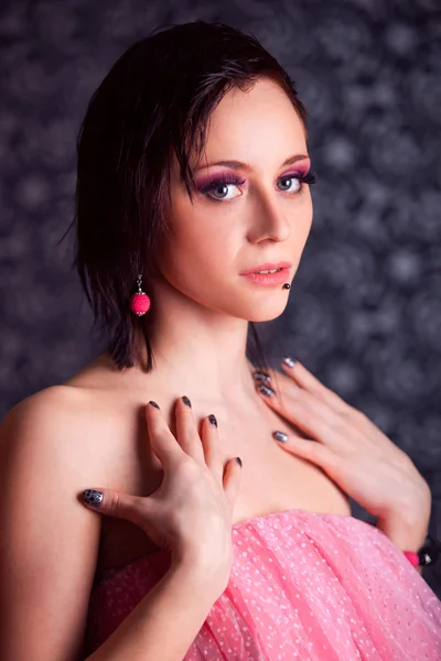 Portrait of a beautiful brunette girl with short hair with red earrings in a black dress on a gray background