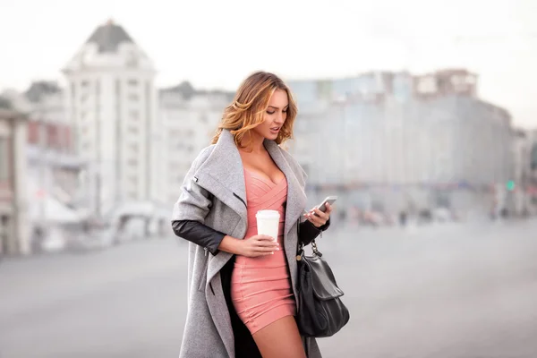 Business and style. A businesswoman checking email via mobile phone and holding a coffee cup against urban scene.